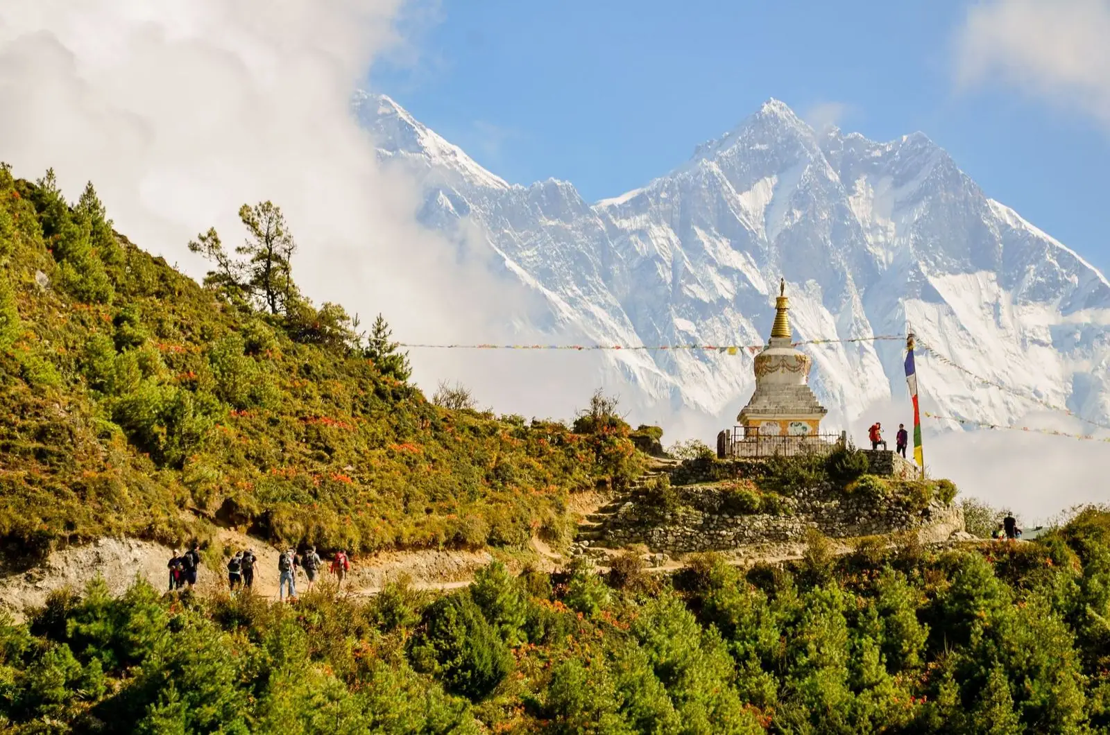 Caminhantes aproximam-se de uma stupa com bandeiras de oração; ao fundo, o Everest e o Lhotse.