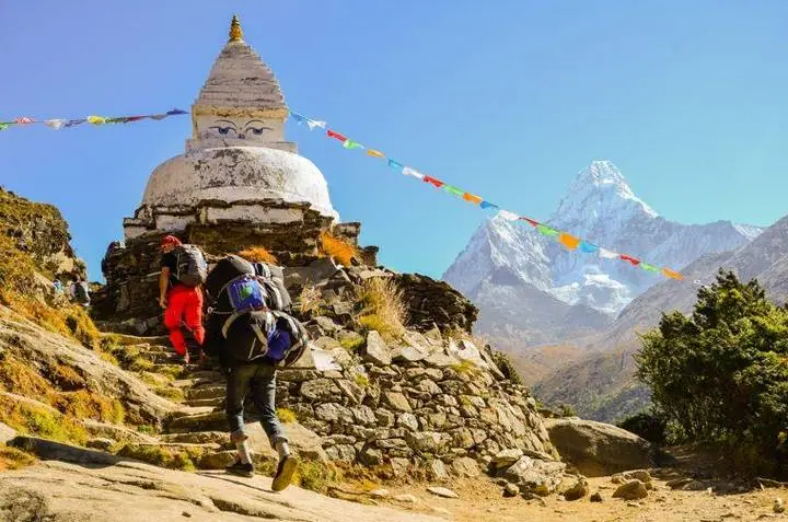Um carregador e um caminhante passam por uma stupa com os olhos de Buda; à direita ergue-se o Ama Dablam.