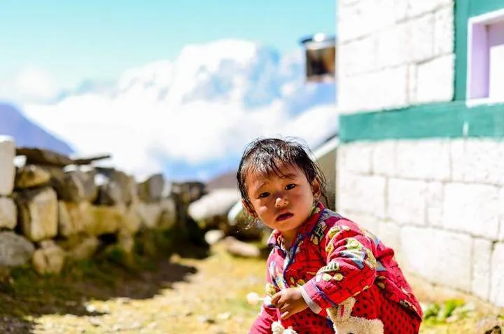 Uma criança numa aldeia do vale do Khumbu, junto a uma casa de pedra caiada.